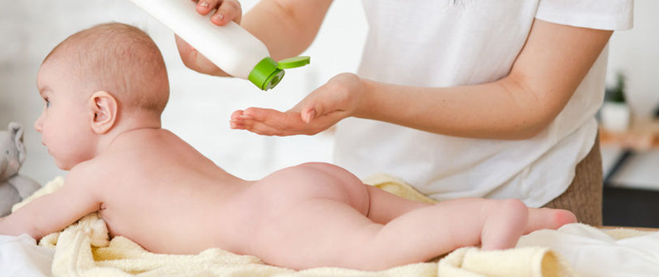 A baby lies on their stomach during a gentle massage, with a caregiver applying lotion from a green bottle, emphasizing a nurturing and calming baby care routine.