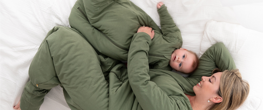 A mother and her baby, both in matching green outfits, lie on a white bed