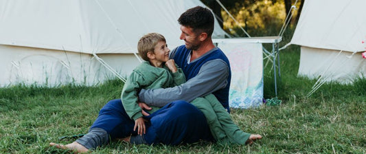 a father and son sitting on the grass, enjoying a moment together while camping