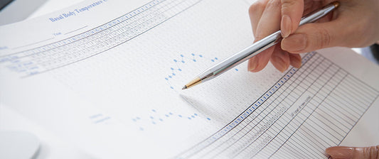 A person marks data on a basal body temperature chart, used for tracking fertility cycles.