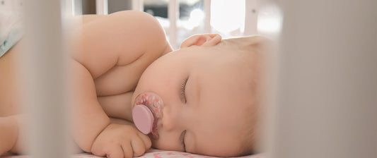  A peaceful baby sleeps with a pacifier, viewed through the slats of a crib, with soft lighting enhancing the serene atmosphere.