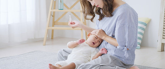 A concerned mother checks her crying baby's temperature with a digital thermometer while comforting them in a softly lit nursery.