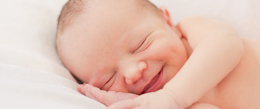 A newborn smiles softly while sleeping on a white blanket, capturing a serene and joyful moment.