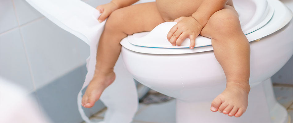  A toddler sits on a toilet with a child-sized seat, feet dangling, as they learn the process of potty training in a bright, clean bathroom.