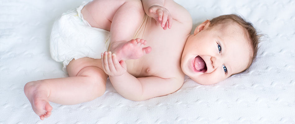 a joyful baby lying on a textured white blanket, happily playing and possibly in the middle of attempting to roll over.