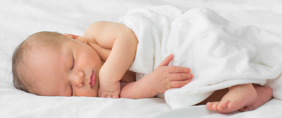  A peaceful newborn sleeps soundly, wrapped in a soft white blanket on a comfortable bed, showcasing the serene and restful state of an infant.