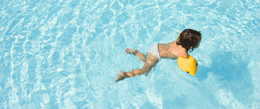 A young child is swimming in a pool, wearing yellow floatation devices on their arms.